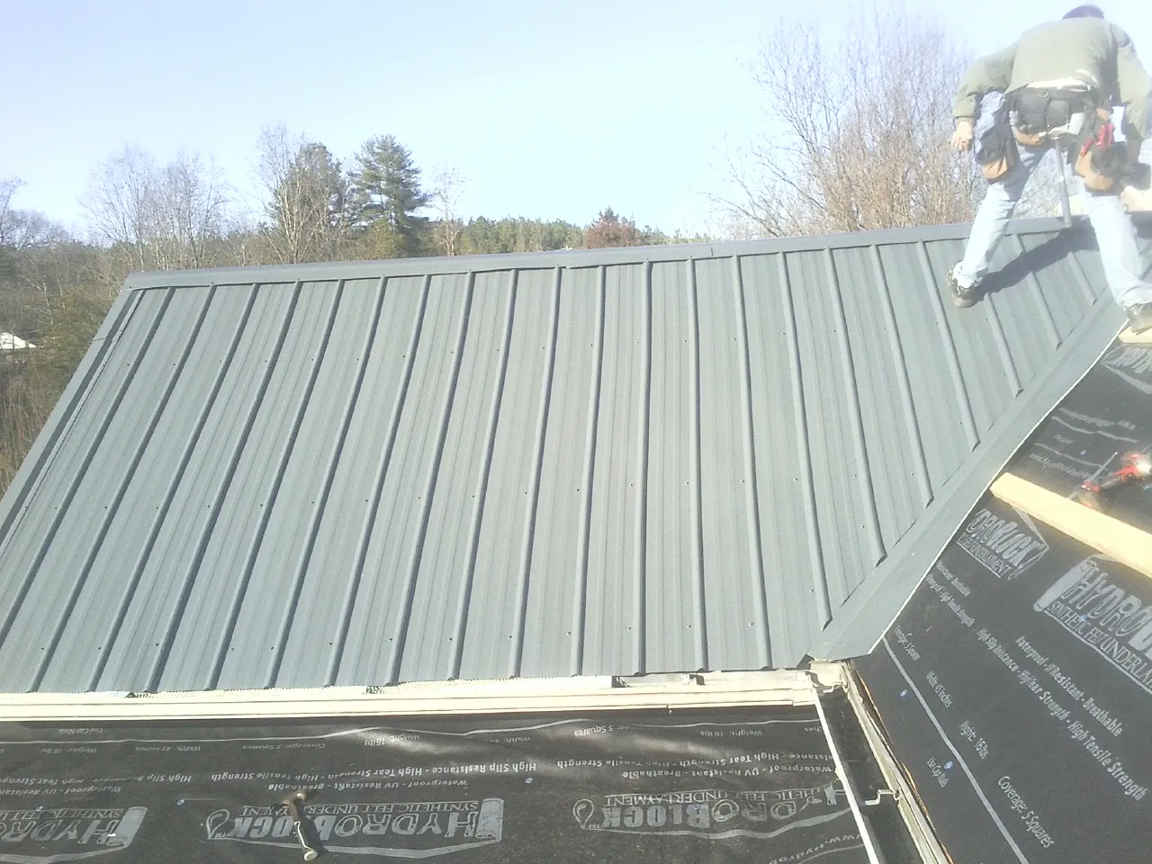 Crew installing dark green standing seam panels over synthetic underlayment in Allenton