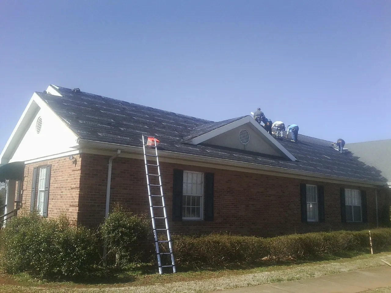 Crew tearing shingles off a brick ranch roof with a ladder set — Emergency Roof Repair work by our crew in Allenton