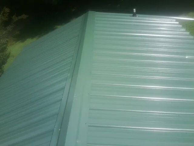 New green metal panels meeting at the ridge of a roof — Flat Roof Repair work by our crew in Allenton