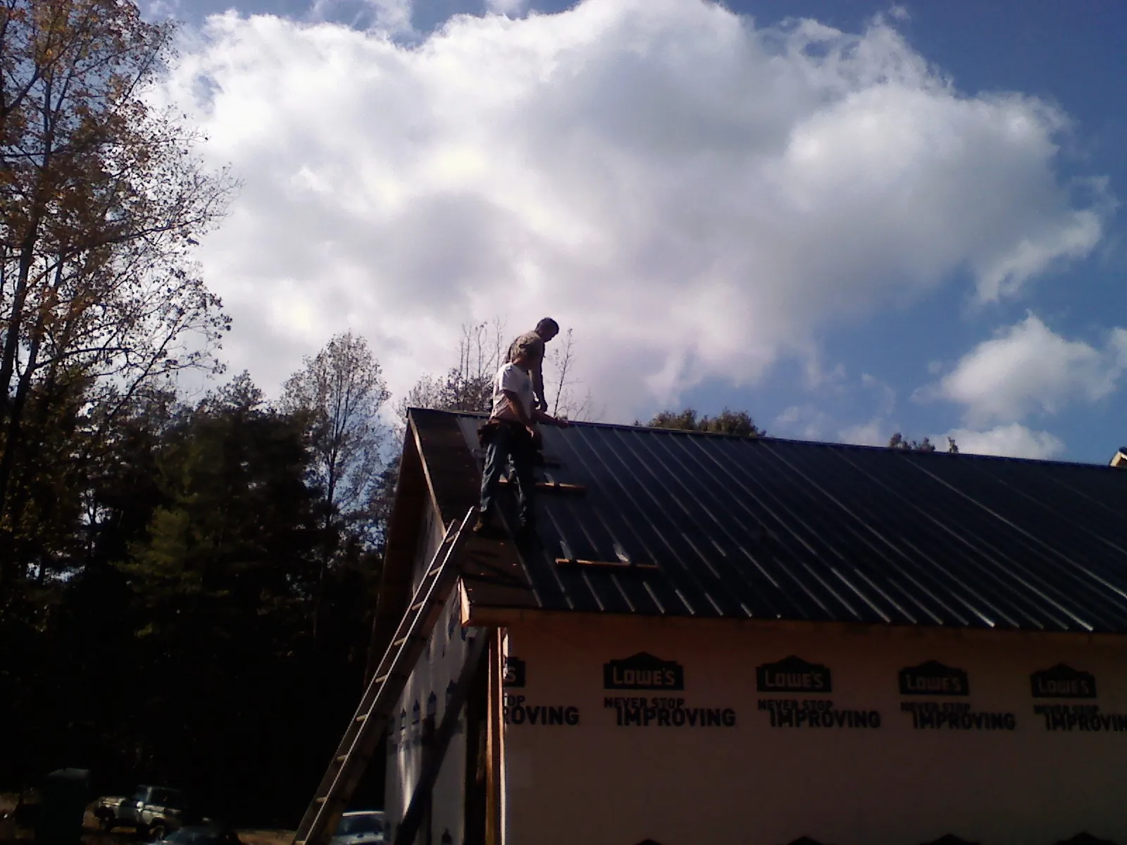 Roofer fastening dark metal panels high against a cloudy sky, from a Roof Inspection job in Allenton