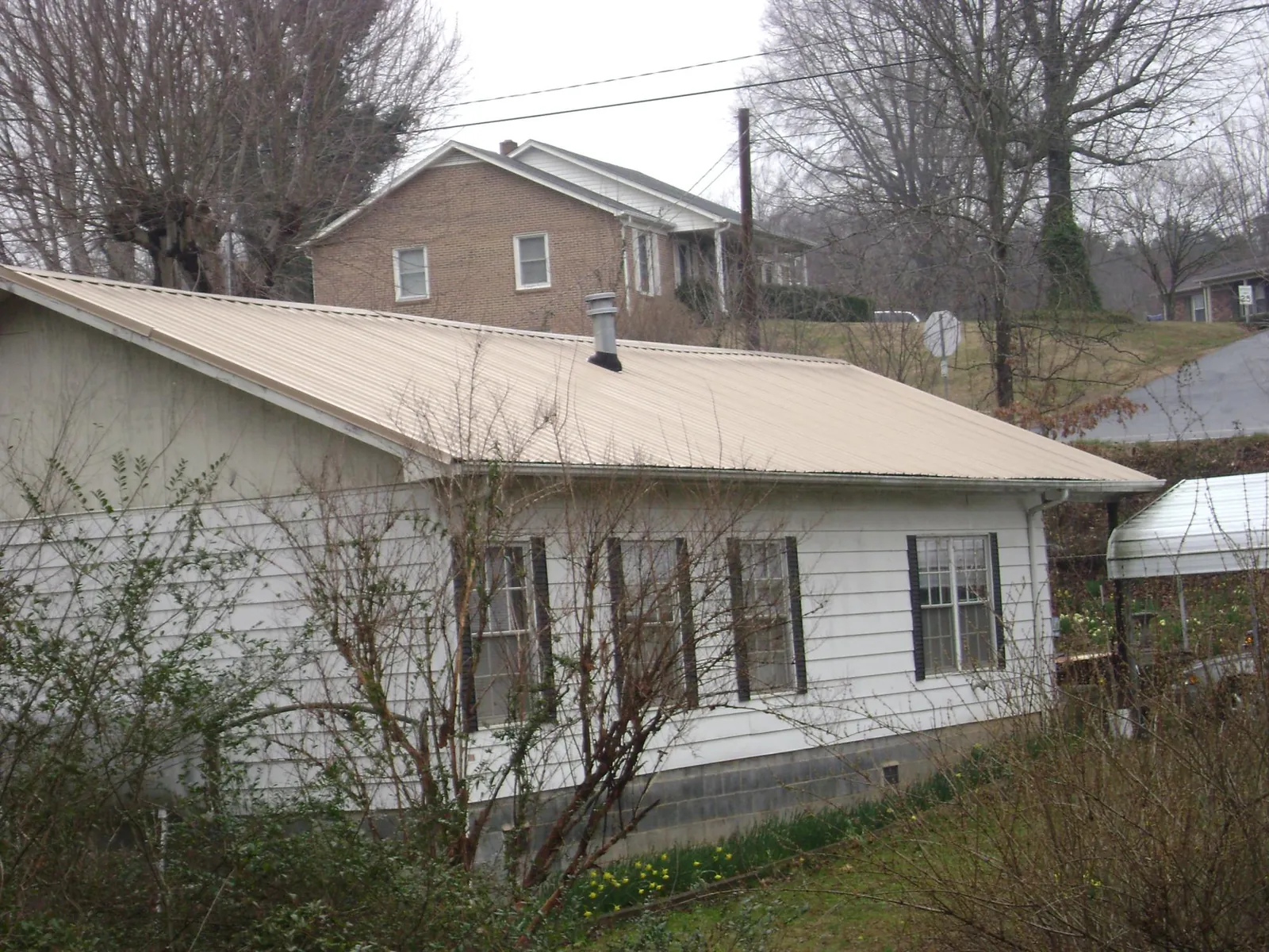 Tan metal roof on a white sided house set into a hillside — Commercial Roofing by Roofing Brothers in Allenton
